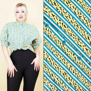 Op de afbeelding: Een vintage overhemd met een uniek patroon. Het overhemd heeft verticale strepen in teal, wit en geel, met zwarte dierenprint accenten. De top met korte mouwen is in de taille geknoopt. Het model draagt een zwarte legging.