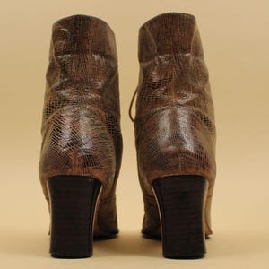 May include: A pair of brown leather ankle boots with a snakeskin pattern. The boots have a block heel and a lace-up front.