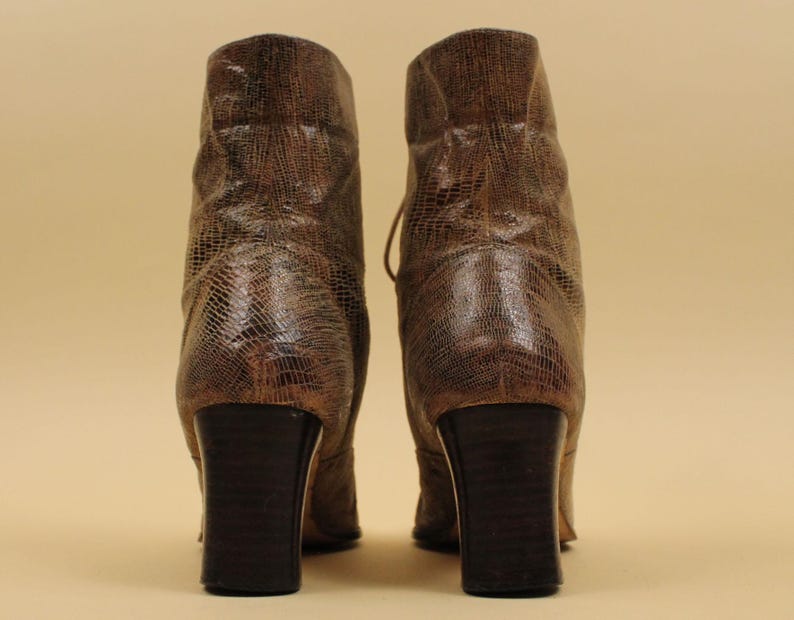 May include: A pair of brown leather ankle boots with a snakeskin pattern. The boots have a block heel and a lace-up front.