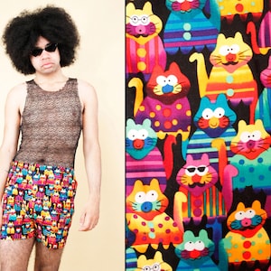 May include: Colorful boxer shorts with a repeating pattern of cartoon cats in various colors and outfits. The shorts are a mix of red, blue, yellow, and green, with a black background. The cats have sunglasses, bow ties, and other accessories.