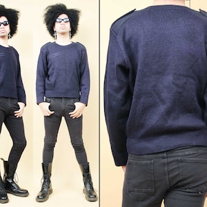 Op de afbeelding: Een donkerblauwe trui met lange mouwen en elleboogpatches. De trui heeft een ronde hals en een geribbelde textuur.