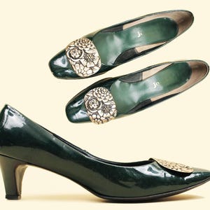 Può includere: Un paio di décolleté in vernice verde con un motivo floreale sulla punta. Le scarpe hanno un tacco basso e sono in buone condizioni.