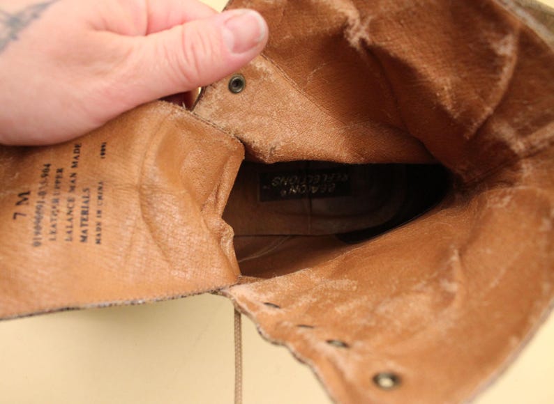 May include: Inside view of a brown leather boot with a lace-up closure. The boot is lined with a soft brown fabric and has a label that reads "Balance Man Made Materials Made in Korea".