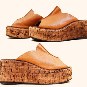 May include: A pair of platform sandals with a cork sole and tan leather upper. The sandals have a unique design with a pointed flap over the foot. The platform sole is approximately 3 inches high.