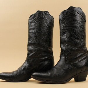 May include: A pair of black leather cowboy boots with intricate embossed designs. The boots have a pointed toe and a low heel.