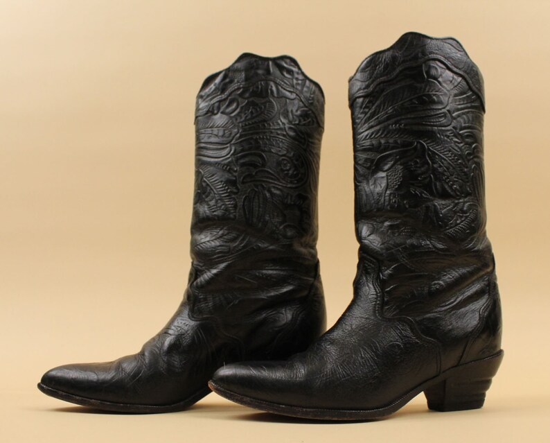 May include: A pair of black leather cowboy boots with intricate embossed designs. The boots have a pointed toe and a low heel.