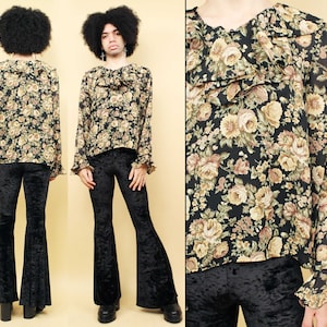 Puede incluir: Una persona lleva una blusa negra de estampado floral con cuello de volantes y mangas largas. También lleva pantalones acampanados de terciopelo negro.