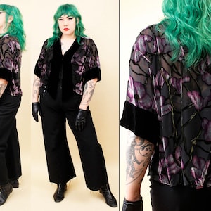 Puede incluir: Una chaqueta negra con estampado floral morado y negro con ribete de terciopelo negro. La chaqueta se combina con pantalones negros y guantes de cuero negros. La chaqueta tiene cuello en V y mangas cortas. El estampado floral es una mezcla de morado y negro.