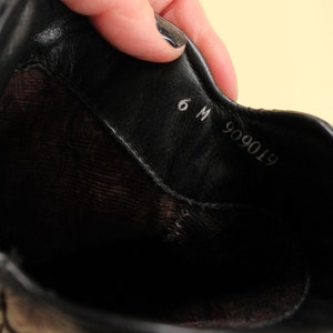 May include: Close-up of the inside of a black leather shoe with the size 6 M and the number 909019 printed on the insole.
