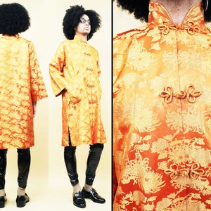 May include: A long, orange and gold brocade robe with a mandarin collar and frog closures. The robe has a floral pattern and is worn by a person with an afro.