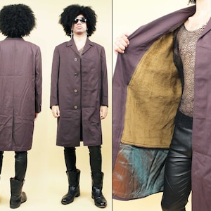May include: A long, dark purple coat with a brown lining. The coat has a button closure and is worn over black pants and boots.