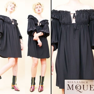 Może przedstawiać: Czarna sukienka bez ramiączek z długimi rękawami i marszczonym dekoltem. Sukienka ma dopasowany gorset i luźną, falującą spódnicę. Sukienka jest wykonana z miękkiej, lekkiej tkaniny. Sukienka jest oznaczona etykietą "Alexander McQueen".