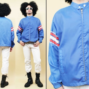 Könnte beinhalten: Eine blaue Nylonjacke mit Reißverschluss und roten und weißen Streifen an den Ärmeln. Die Jacke hat einen Stehkragen und einen einzigen Knopf am Hals.