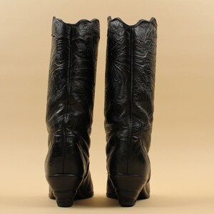 May include: A pair of black leather cowboy boots with intricate floral embroidery. The boots have a pointed toe and a low heel.