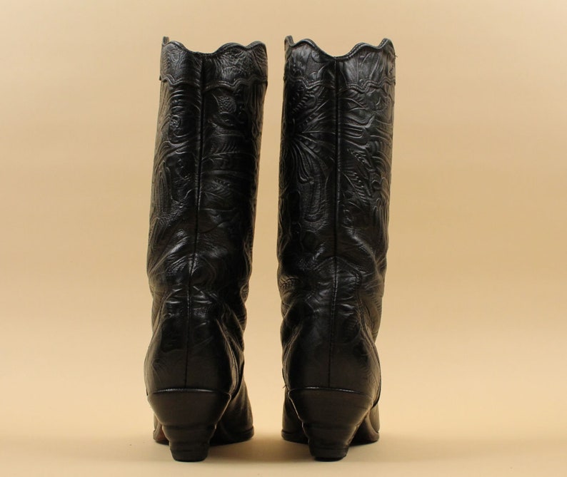 May include: A pair of black leather cowboy boots with intricate floral embroidery. The boots have a pointed toe and a low heel.