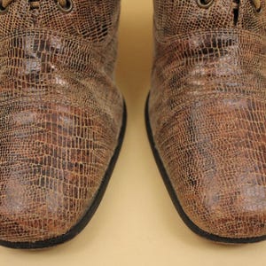 May include: A pair of brown leather boots with a textured, snake-like pattern. The boots have laces and a pointed toe.