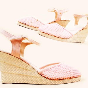 May include: Two pairs of pink espadrille wedge sandals. The sandals have a woven beige wedge heel and a pink mesh upper. The ankle straps and the trim are a solid pink. The sandals are displayed on a light beige background.