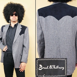 Peut inclure: Un blazer en tweed gris avec des accents en daim noir sur les épaules et le dos. Le blazer a une fermeture à bouton unique et une étiquette qui indique "Brad Whitney".