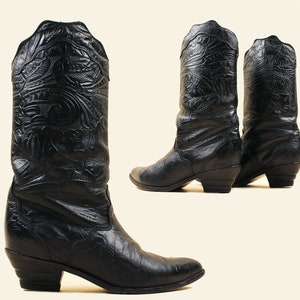 May include: A pair of black leather cowboy boots with intricate embossed designs. The boots have a pointed toe and a low heel.