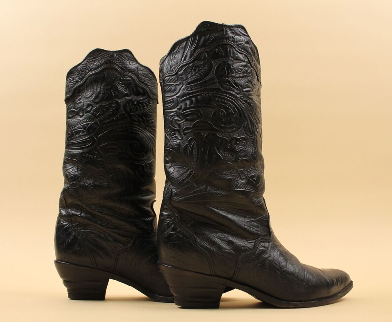 May include: A pair of black leather cowboy boots with intricate embossed patterns. The boots have a pointed toe and a low heel.