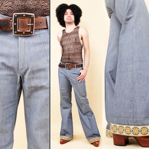Puede incluir: Pantalones acampanados azul claro con un ribete decorativo en el dobladillo. Los pantalones tienen una cintura alta y una pernera ancha. Se ve un cinturón de cuero marrón con una hebilla cuadrada grande. Los pantalones se combinan con zuecos marrones.