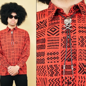 May include: A red and black patterned button-up shirt with a silver skull bolo tie. The shirt has a geometric pattern.