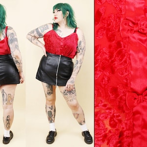 May include: A red camisole top and a black leather mini skirt. The camisole has thin straps and a textured fabric. The skirt has a front zipper. The image also shows a close-up of a red fabric with a floral pattern and bows.