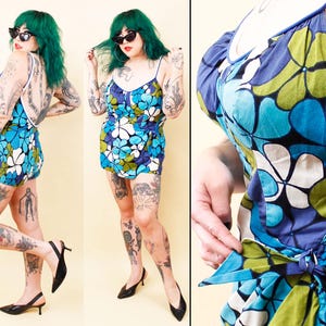 Op de afbeelding: Een vintage romper met bloemenpatroon in blauw, wit en groen. De romper heeft dunne bandjes, een V-hals en een strik in de taille. De lichte stof is geschikt voor warm weer. De outfit wordt gecompleteerd met zwarte hakken. Het ontwerp doet denken aan de jaren 1960.