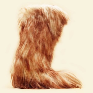 Puede incluir: Un par de botas de piel suave de color marrón y blanco. Las botas están hechas de un material suave y mullido y tienen una punta larga y puntiaguda.