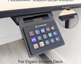 May include: A black foldaway under-desk mount for an Elgato Stream Deck, featuring a hinged bracket that attaches to a desk edge. The device has fifteen square keys with various illuminated icons, including media controls and gaming symbols.
