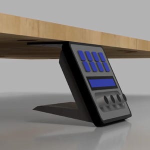 Könnte beinhalten: Eine schwarze und graue Steuereinheit für unter den Schreibtisch mit einer schrägen Oberfläche, acht rechteckigen blauen Tasten, einem zentralen blauen horizontalen Display und vier runden schwarzen Drehknöpfen am unteren Bedienfeld.