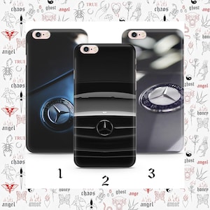May include: Three black phone cases featuring Mercedes-Benz car designs. The cases display the Mercedes-Benz logo and car details in silver and black. The background has a repeating pattern of tattoos with words like "chaos" and "angel".
