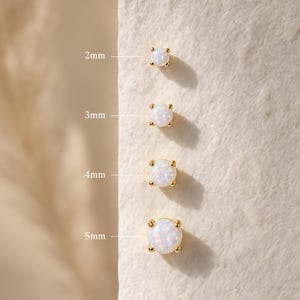 May include: Four round opal stud earrings set in gold prongs, arranged vertically by size. The labels indicate diameters of 2mm, 3mm, 4mm, and 5mm. Each earring features a white iridescent stone with subtle flashes of color held by four gold prongs.