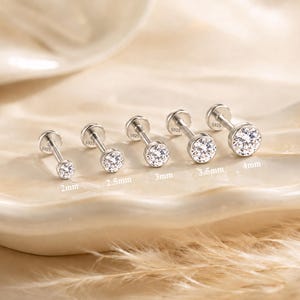 May include: Five silver-tone stud earrings with clear round stones in bezel settings, arranged by size from 2mm to 4mm. Each post is stamped with S925. The earrings are displayed in a row, showing graduated diameters for each individual piece.