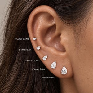 May include: Five silver-toned pear-shaped stud earrings arranged in a row on an earlobe and cartilage. The sizes are labeled as 2*3mm-0.12ct, 3*4mm-0.3ct, 3*5mm-0.35ct, 4*6mm-0.5ct, and 5*7mm-0.8ct, showing the scale of each individual stone.