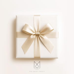 May include: A square, white gift box with a champagne-colored satin ribbon and bow. The bow is centered on the top of the box, with the ribbon wrapped around the box. The background is a soft, off-white color. The text "SOFT LIGHT MOCKUP" and "PSD SMART OBJECT" is at the bottom.