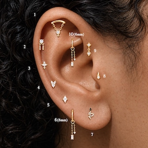 May include: A collection of ten gold-toned ear piercings featuring various designs, including small hoops with dangling chains, studs with clear crystals, and a snake-shaped stud. The jewelry pieces are numbered 1 through 10, with sizes 6mm and 8mm noted.