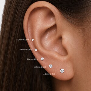 May include: Five round stud earrings arranged in a vertical line along the ear cartilage and lobe. The sizes are labeled as 2.0mm-0.03ct, 2.5mm-0.06ct, 3.0mm-0.1ct, 3.5mm-0.2ct, and 4.0mm-0.3ct, showing the progression of the clear stones.