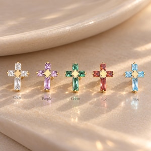 May include: Five gold-toned cross-shaped stud earrings, each featuring four baguette-cut gemstones arranged in a cross pattern with a central gold star accent. The stones are clear, purple, green, red, and blue, labeled respectively below each.