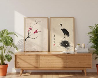 以下が含まれることがあります： 日本の美学を持つ2つの額入りアートプリント。1つはピンクの花が咲く枝、もう1つは卵のある巣の中にいる黒い鶴が特徴です。どちらのプリントもベージュの背景で、木製のフレームに入っています。プリントは木製のキャビネットに飾られています。