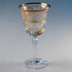 May include: A clear wine glass with a gold rim and a decorative etched floral design. The upper portion of the glass is amber-colored, while the lower portion features a diamond-cut pattern. The stem and base are clear.