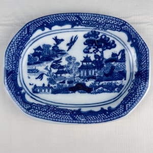May include: Blue and white oval serving dish with a detailed landscape scene. The dish features a decorative border and a central image of pagodas, trees, and birds. A classic piece for serving appetizers or small dishes.