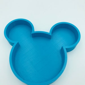 Pu&ograve; includere: Un vassoio blu a forma di Mickey Mouse. Il vassoio &egrave; realizzato in un materiale blu chiaro e presenta le iconiche orecchie del topo. Il vassoio &egrave; progettato con un fondo piatto e bordi rialzati. Lo sfondo &egrave; bianco.