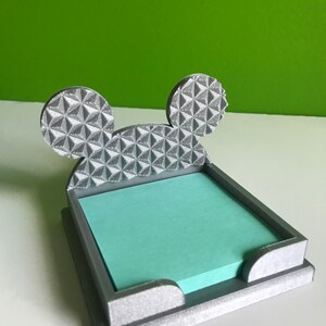 Op de afbeelding: Een grijze 3D-geprinte bureau-organizer in de vorm van Mickey Mouse-oren. De oren zijn getextureerd met een geometrisch patroon. De organizer heeft een gleuf om sticky notes in te bewaren.