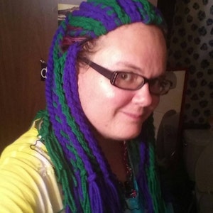 May include: A person with long, green and purple yarn hair extensions. The hair is styled in a straight, flowing style. The person is wearing a yellow shirt and a blue and white patterned shirt underneath.