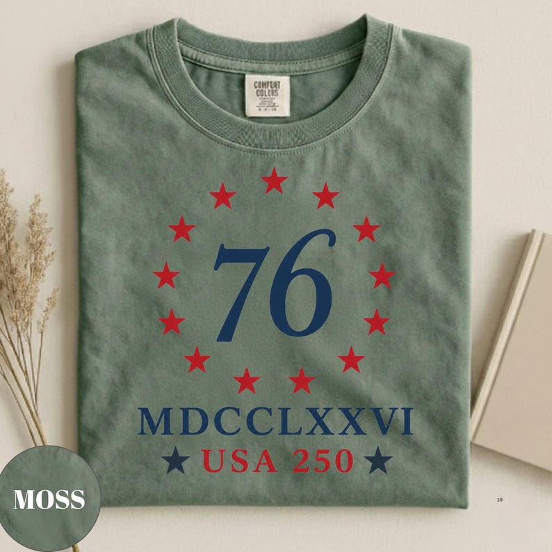 Op de afbeelding: Mosgroen T-shirt met ronde hals. De voorkant toont een marineblauwe "76" omringd door rode sterren, met "MDCCLXXVI" en "USA 250" eronder. Het shirt heeft een vintage, versleten uitstraling.