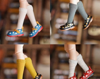 May include: Four pairs of doll shoes with different colored polka dots and socks. The shoes are black with a gold buckle and a white polka dot pattern. The socks are white, gray, yellow, and red.