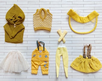 May include: A set of yellow and white doll clothes, including a hooded sweater, a vest, a pair of overalls, a skirt, a pair of leggings, a visor, and a pair of socks.