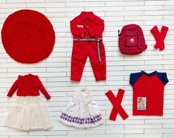 May include: A set of red and white doll clothes, including a red jumpsuit, a red sweater, a white skirt, a white dress with red and blue accents, a red and blue striped shirt, a red beret, a red backpack, and red socks.