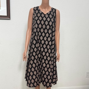May include: A sleeveless knee-length dress featuring a black base with a repeating tan leaf-like pattern. The garment has a V-neckline and a relaxed, flowing silhouette that hangs straight from the shoulders, providing a simple and consistent look.